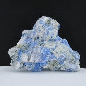 May include: A close-up of a mineral specimen with a rough, irregular shape. The stone features a mix of blue, white, and gray hues, with a crystalline texture. The background is black and white, highlighting the mineral's natural beauty.