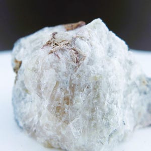 May include: A raw, crystalline mineral specimen featuring a translucent white and off-white structure with visible jagged edges and small patches of brown inclusions embedded within the rough, multifaceted surface of the stone.