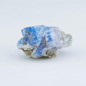 May include: A raw mineral specimen featuring vibrant blue crystalline structures integrated with translucent white and pale grey rocky matrix. The cluster displays sharp, angular facets and varying levels of opacity across its irregular, jagged surface.