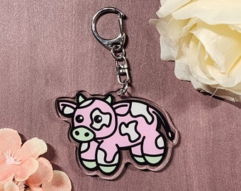 Könnte beinhalten: Ein rosa-weißer Kuh-Schlüsselanhänger mit einem silbernen Schlüsselring. Die Kuh hat schwarze Augen und eine schwarze Nase.