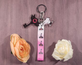 Könnte beinhalten: Ein rosa-weißer Schlüsselanhänger in Schlüsselform mit einer schwarz-weißen Comicfigur darauf. Der Schlüsselanhänger hat einen silbernen Schlüsselring und eine schwarz-weiße Comicfigur darauf.