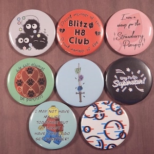 May include: Set of 8 round button pins with various designs. The pins feature cartoon characters, text, and abstract patterns. The pins are black, white, red, blue, green, and pink.