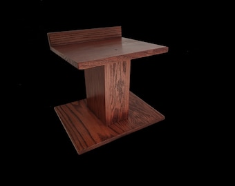 May include: A dark brown wooden speaker stand with a rectangular top and bottom shelf. The stand is made of solid wood and has a natural wood grain finish.