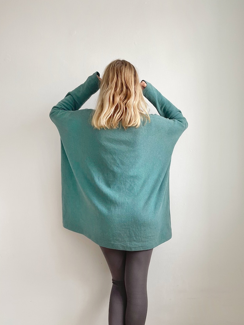 May include: An oversized teal blue sweater with long sleeves. The sweater is being worn by a person with blonde hair and is paired with dark grey leggings.