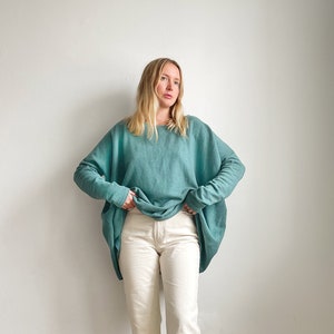 May include: A woman wearing a teal blue oversized sweater with long sleeves and white straight-leg jeans.