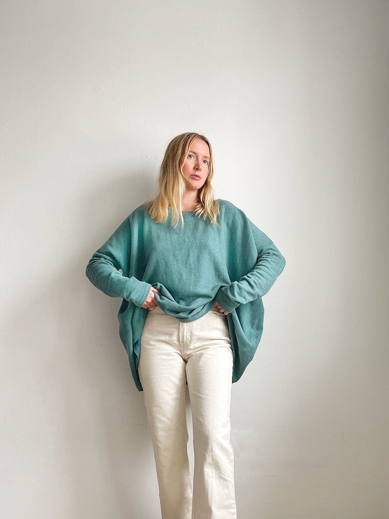 May include: A woman wearing a teal blue oversized sweater with long sleeves and white straight-leg jeans.