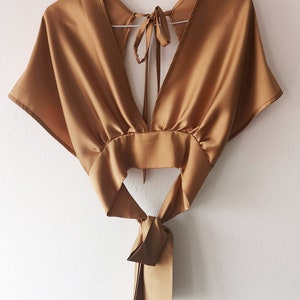 Pu&ograve; includere: Un top in satin dorato con scollo a V profondo e un nodo sul retro.