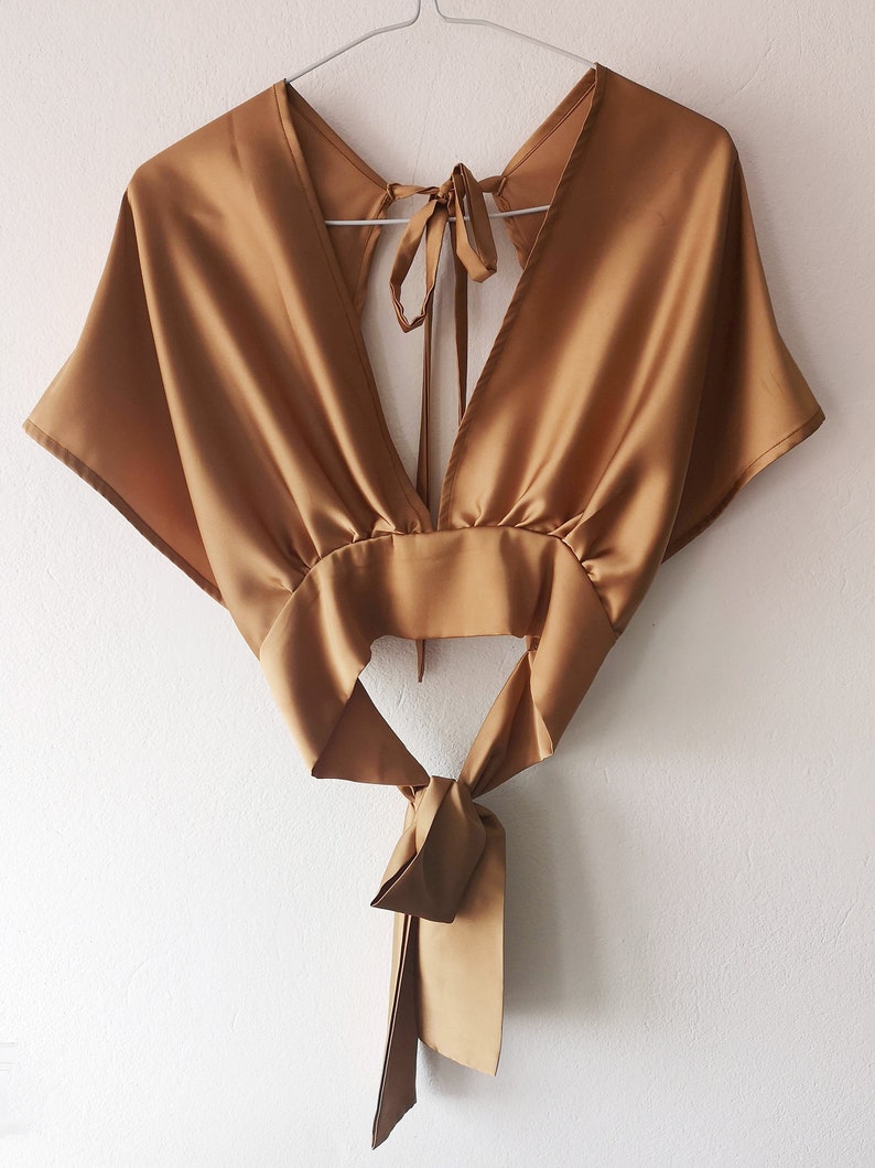 Pu&ograve; includere: Un top in satin dorato con scollo a V profondo e un nodo sul retro.