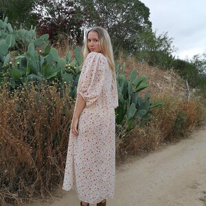 May include: A woman wearing a white maxi dress with a floral print. The dress has a loose fit and a gathered neckline. She is wearing brown ankle boots.
