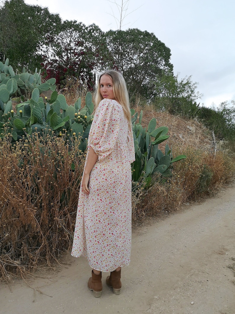 May include: A woman wearing a white maxi dress with a floral print. The dress has a loose fit and a gathered neckline. She is wearing brown ankle boots.