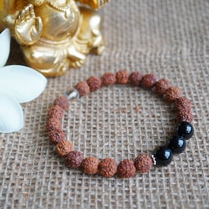 May include: A brown and black beaded bracelet with a silver clasp. The bracelet has three black beads at the end.