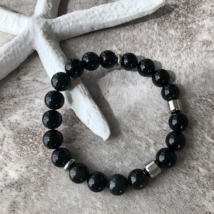 May include: A black beaded bracelet with silver metal accents. The bracelet is made of round, smooth beads.