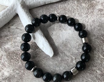 May include: A black beaded bracelet with silver metal accents. The bracelet is made of round, smooth beads.
