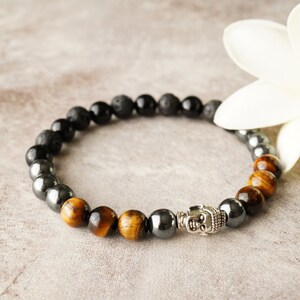 May include: A beaded bracelet with black lava rock, tiger's eye, and hematite beads. A silver Buddha charm is in the center of the bracelet.