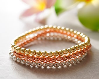 May include: Three stacked bracelets with gold, rose gold, and silver beads. The bracelets are made of small, round beads.