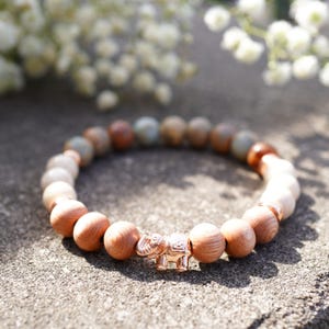 May include: A brown wooden beaded bracelet with a rose gold elephant charm. The beads are interspersed with light brown and white stones.
