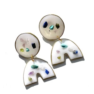 May include: White resin earrings with gold accents and embedded colorful gemstones. The earrings are shaped like a circle with a half-circle attached.