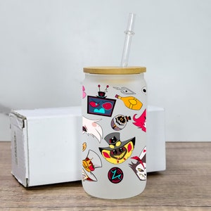May include: A white frosted glass tumbler with a bamboo lid and a clear drinking straw. The tumbler is decorated with colorful cartoon characters and designs, including a red-eyed robot, a yellow character with a top hat, and a white character with wings.