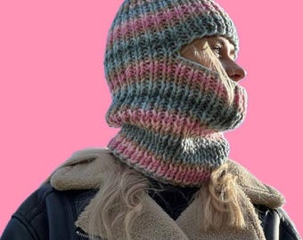 May include: A gray and pink striped knit balaclava with a hole for the eyes and mouth. The balaclava is worn by a person with blonde hair and a black leather jacket.