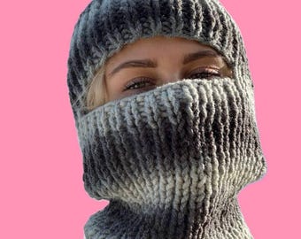 May include: A gray and white knit balaclava with a hole for the eyes. The balaclava is made of a soft, chunky yarn.