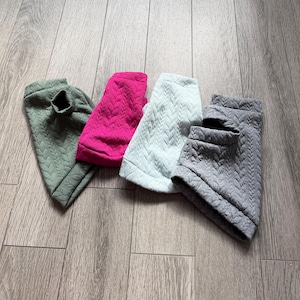 May include: Four pet sweaters in olive green, bright pink, light blue, and charcoal gray. Each sweater features a textured, quilted cable knit pattern, a ribbed collar, and a sleeveless design, providing a consistent look across all four items.