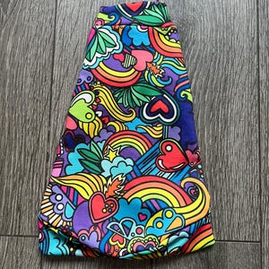 May include: A colourful fabric with a psychedelic pattern featuring rainbows, hearts, and swirls in shades of pink, yellow, blue, green, and purple.