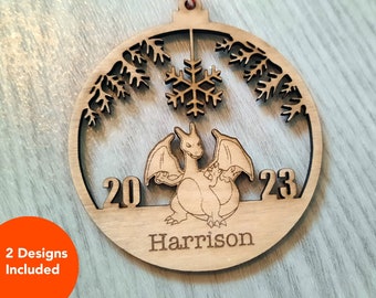 May include: A wooden Christmas ornament shaped like a circle with a snowflake, pine branches, and a cartoon dragon inside. The ornament has the numbers 20 and 23 on either side of the dragon and the name "Harrison" at the bottom.