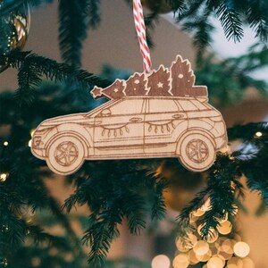 May include: A wooden Christmas ornament shaped like a car with a Christmas tree on top. The car is brown and has a white string hanging from it.