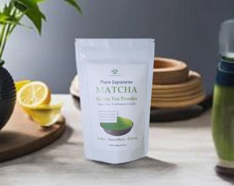May include: A white pouch of Pure Japanese Matcha Green Tea Powder. The pouch has a green illustration of matcha powder in a bowl. The text on the pouch says "Superior Culinary Grade". The background includes a black vase, lemons, and a green bottle.