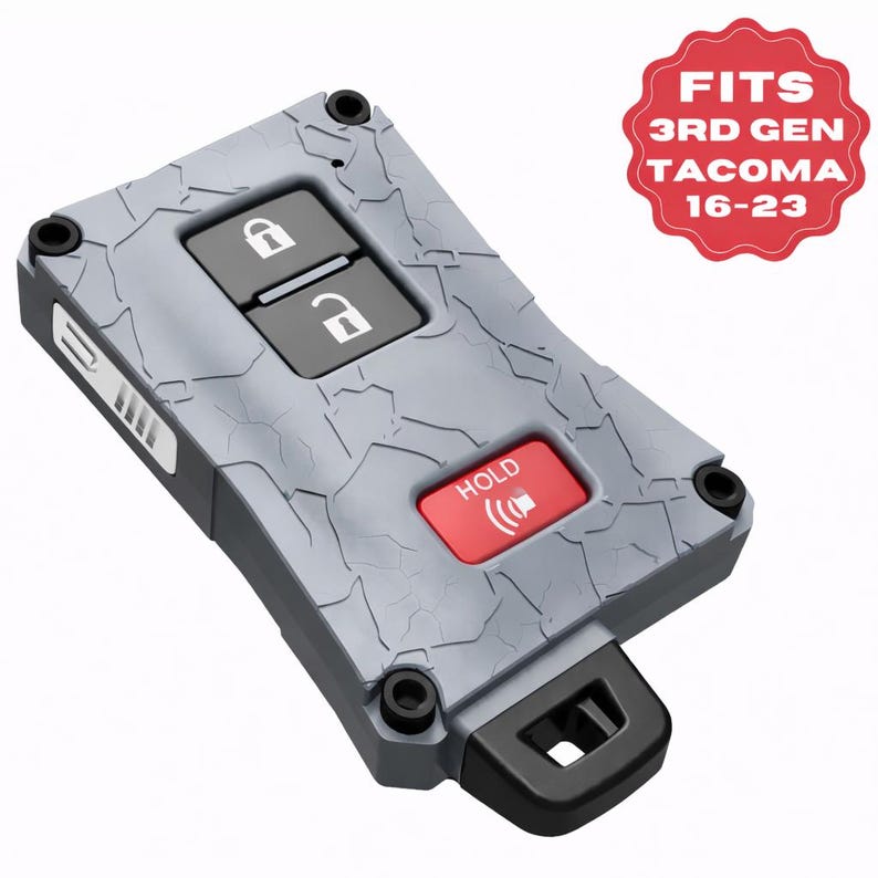 May include: Gray key fob cover with a textured surface, featuring black buttons for lock and unlock, and a red "HOLD" button. The cover has a key ring loop and the text "FITS 3RD GEN TACOMA 16-23" on a red badge.
