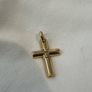 May include: A gold-colored cross pendant with a simple, classic design. The cross has a vertical bar and a horizontal bar, forming the traditional Christian symbol. The pendant is likely made of metal and has a shiny finish.