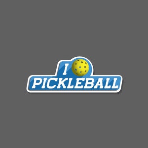 May include: A blue and white sticker with the words "I PICKLEBALL" and a yellow pickleball. The sticker has a white border and a shadow effect, and is set against a gray background.