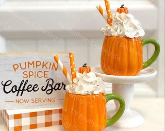 Puede incluir: Dos tazas de café de especias de calabaza con crema batida y pajitas. Las tazas son de color naranja y tienen forma de calabaza. El letrero dice "Pumpkin Spice Coffee Bar - Now Serving".