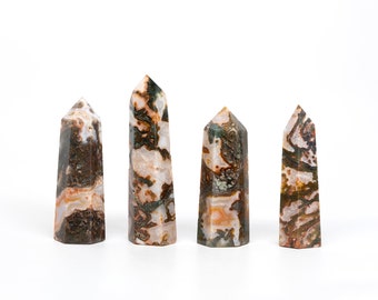 May include: Four brown, white, and green agate crystal points arranged in a row on a white surface.