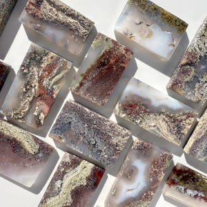 May include: A collection of 12 agate slices with a variety of colors and patterns, including red, brown, white, and gray. The slices are all rectangular in shape and have a smooth, polished surface.