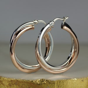 以下が含まれることがあります： トリコロールデザインのフープピアス。シルバー、ローズゴールド、ゴールドの組み合わせです。フープは丸く、光を反射する研磨仕上げです。ゴールドカラーの表面に展示されています。