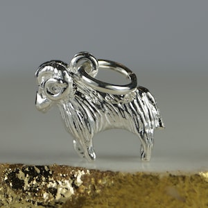 May include: A detailed silver ram charm, with textured fur and curled horns. The charm has a loop for attaching to a necklace or bracelet. The ram is a symbol of the zodiac sign Aries.