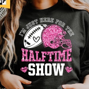 May include: A black sweatshirt with a pink glitter design that says "I'm just here for the halftime show" with a football and helmet graphic.
