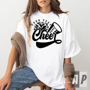 Peut inclure: T-shirt blanc surdimensionn&eacute; avec un graphique noir d'un pompon de pom-pom girl et d'un m&eacute;gaphone avec le texte "Your Text Name Cheer".