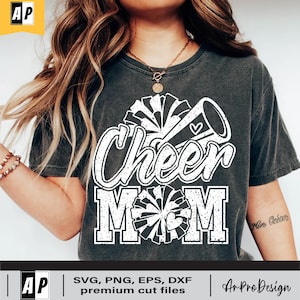 Może przedstawiać: Szary T-shirt z białym nadrukiem, na kt&oacute;rym widnieje napis "Cheer Mom" z megafonem cheerleaderki i pomponami.