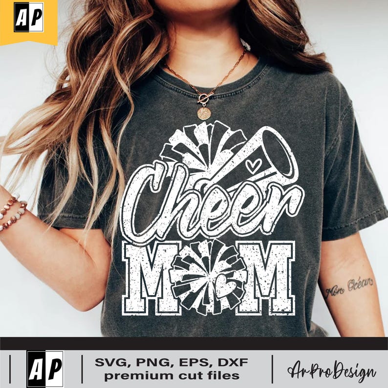 Może przedstawiać: Szary T-shirt z białym nadrukiem, na kt&oacute;rym widnieje napis "Cheer Mom" z megafonem cheerleaderki i pomponami.