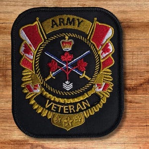 Puede incluir: Parche bordado negro con borde dorado y las palabras "ARMY VETERAN". El parche presenta un emblema central con espadas cruzadas, una corona y hojas de arce, con banderas rojas y blancas a cada lado.