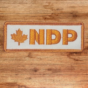 May include: A white patch with a brown border and a gold embroidered maple leaf and the text "NDP".