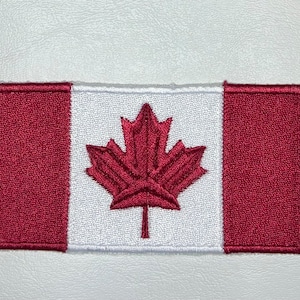 Peut inclure: Un écusson brodé représentant le drapeau canadien avec une feuille d'érable rouge sur fond blanc.