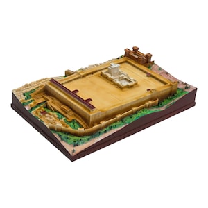 May include: A detailed scale model of an ancient temple complex featuring a central white structure, tan courtyards, and surrounding stone walls with reddish-brown roofs. The base includes green landscaping and textured terrain details.