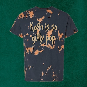Pu&ograve; includere: T-shirt blu navy con effetto scolorito e sbiancato. Il testo "Korn is so girly pop" &egrave; stampato in stile manoscritto. Il design &egrave; di colore marrone chiaro.