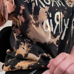 Pu&ograve; includere: T-shirt nero e beige tie-dye con la scritta argentata "Korn's Girly". Abbinato a pantaloncini neri con un disegno di filo spinato bianco.