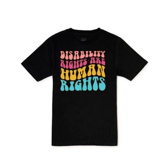 May include: Black t-shirt with the text "DISABILITY RIGHTS ARE HUMAN RIGHTS" in a retro, colorful font. The text is layered in pink, yellow, and blue. The shirt is a short-sleeved crew neck.