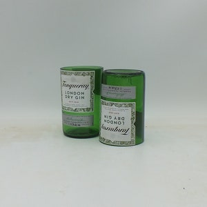 May include: Two empty green glass bottles with the label "Tanqueray London Dry Gin" on them. The bottles are sitting on a white surface.