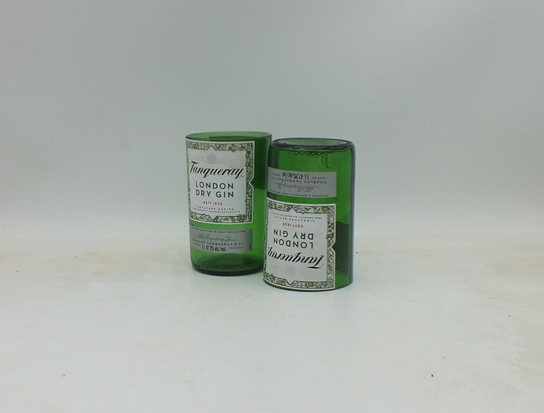 May include: Two empty green glass bottles with the label "Tanqueray London Dry Gin" on them. The bottles are sitting on a white surface.